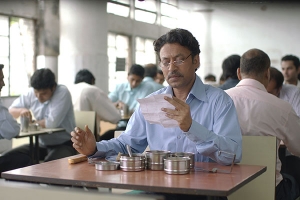 a man in a blue shirt, sits at a table with his lunch, while holding up a letter