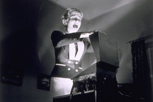 a blonde woman screaming as she opens a box on a table with light shining out of it